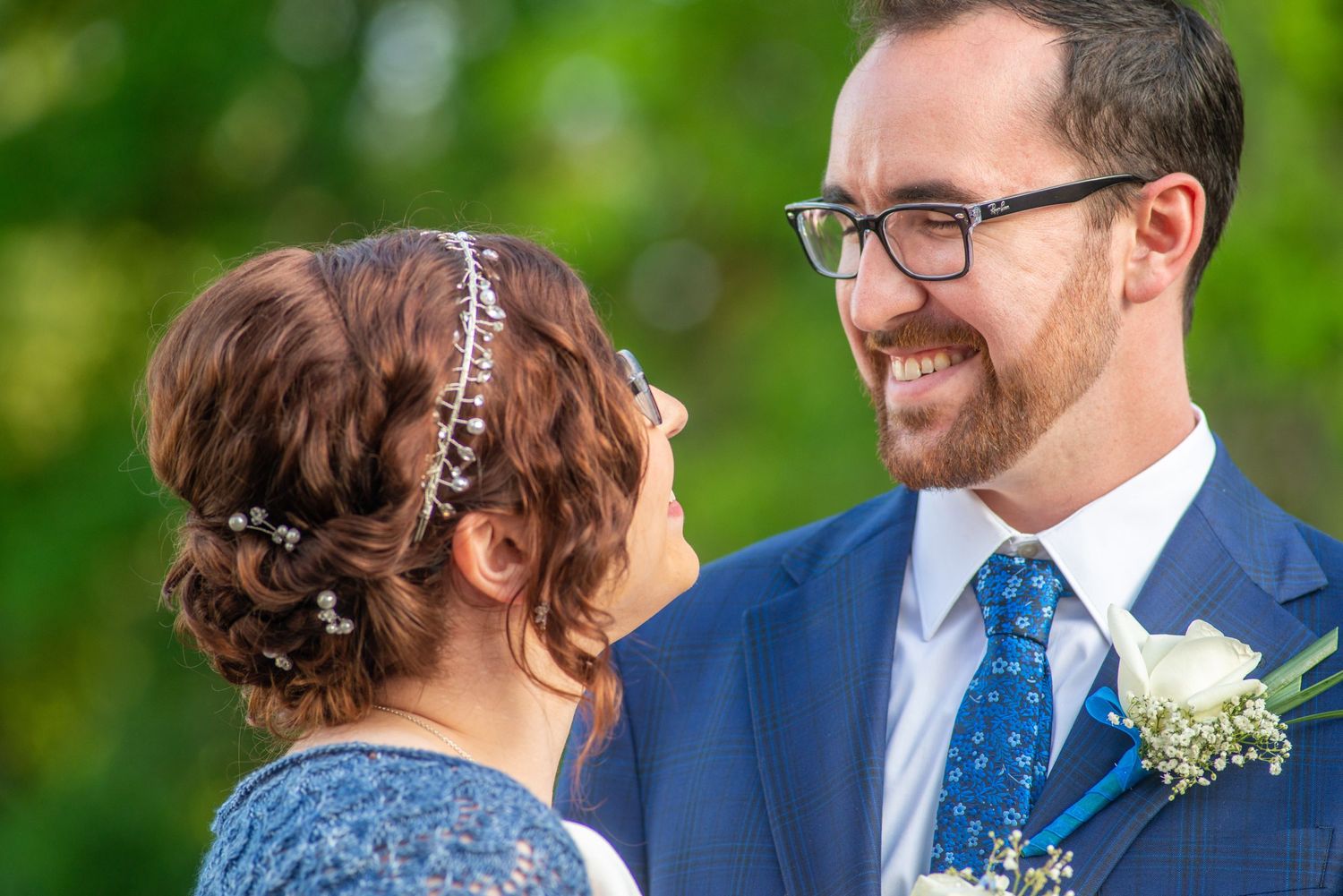 Two newlyweds in blue attire share a joyful moment outdoors with natural greenery in the background.