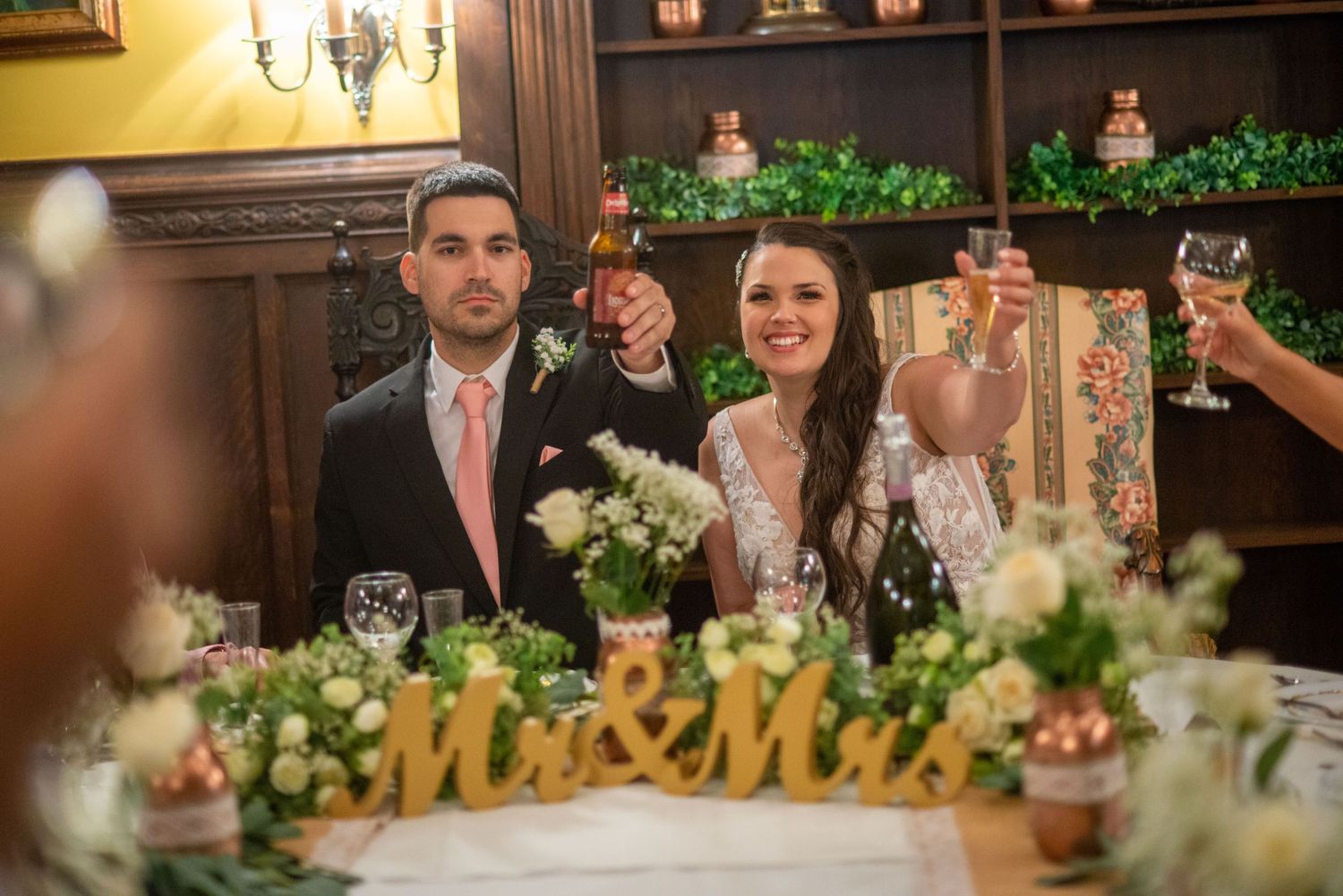 Wedding reception table decorated with greenery, floral centerpieces and 'Mr & Mrs' signage.