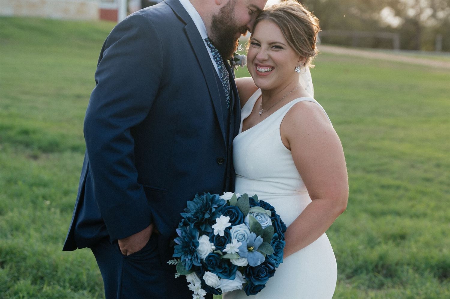Newlyweds sharing tender moment with blue bouquet in outdoor setting.