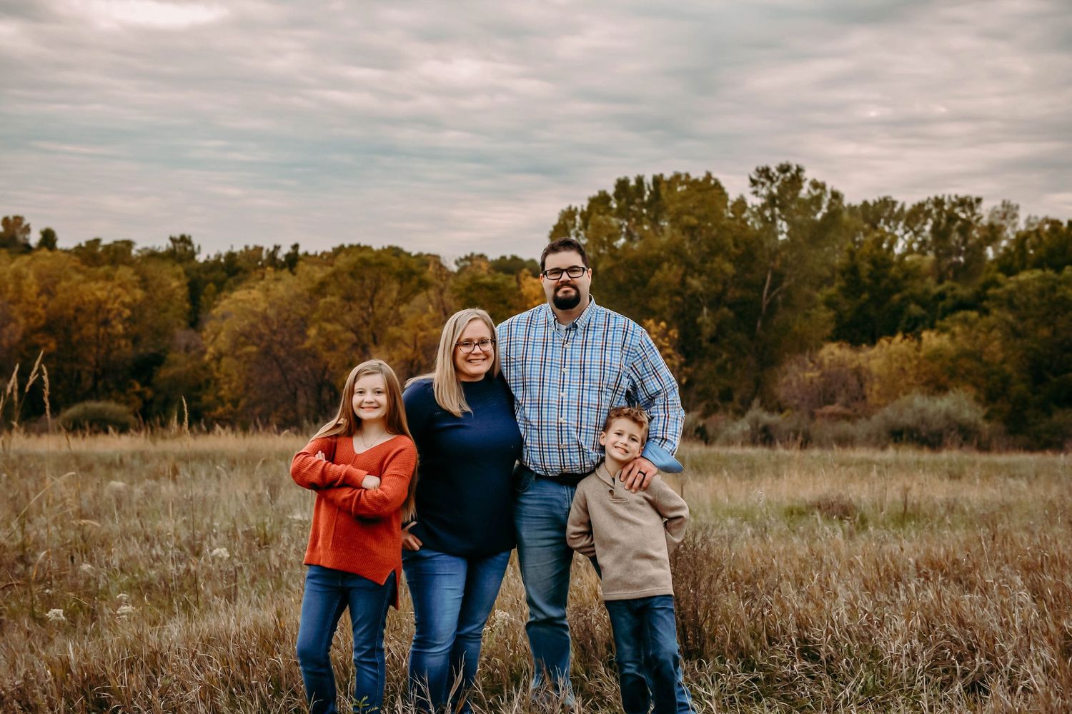 family standing in field with tree line behind them