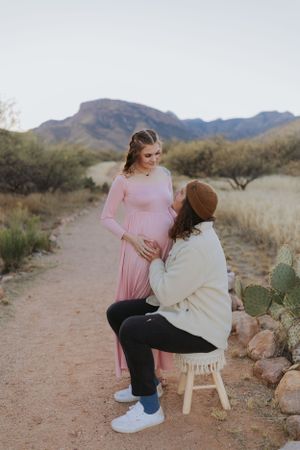 A tender moment captured between two people sitting on a wooden stool in a desert setting.