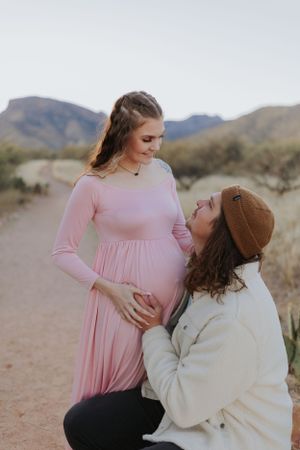 A couple embraces while sitting together in a desert setting with mountains visible in the distance.