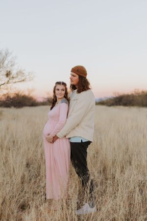 A romantic desert photoshoot featuring two people in pink and cream outfits against golden grass.