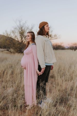 Two people hold hands while walking through tall desert grass at sunset.