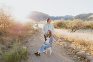 A couple shares a tender moment while seated on a wooden chair in the desert.