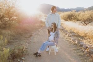 A couple poses together on a desert path with mountains and sunset in the background.