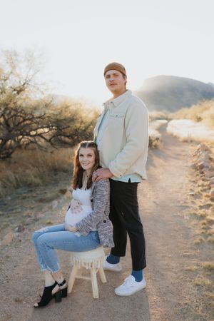 A couple sits on a wooden chair in a desert setting during golden hour.