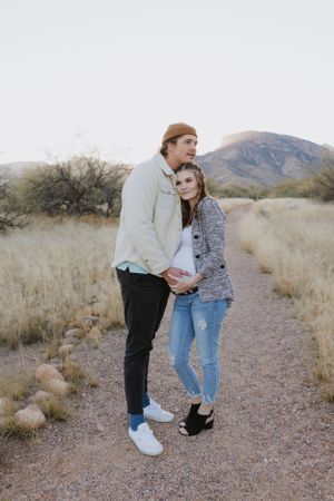 Two people share a sweet moment on a gravel path with desert mountains in the background.