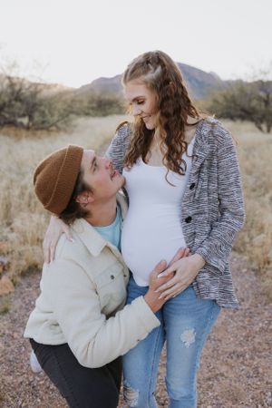A touching maternity photo session in a desert landscape with mountains visible.