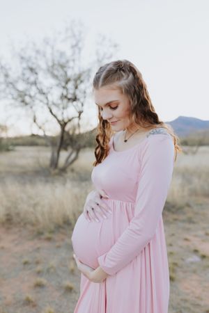 A person in a pink maternity dress poses against a desert backdrop during golden hour.