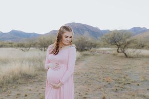 A maternity photo featuring a flowing pink dress in a desert setting.