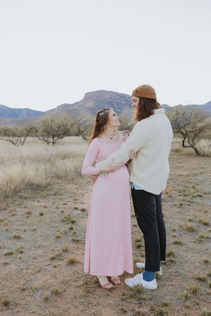 A couple's maternity photoshoot in the desert with mountains and brush in the background.