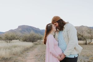 A tender moment between a couple on a desert path with mountains visible behind them.