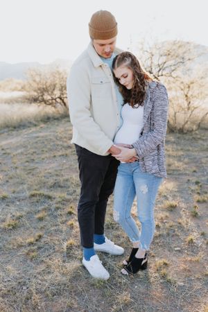 A couple poses together on a desert trail during golden hour, wearing casual outfits.