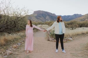 Two people walking hand in hand on a desert trail with mountains in the background.