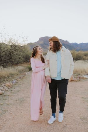 Two people laughing together while walking on a desert path with mountains behind them.