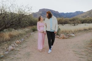 A couple walking together on a desert trail with mountains and brush in the background.