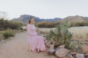A pink dress flows in the desert breeze as a couple stands among cacti and rocks.
