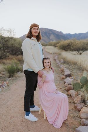 Two people share an intimate moment on a small wooden stool against a desert landscape.
