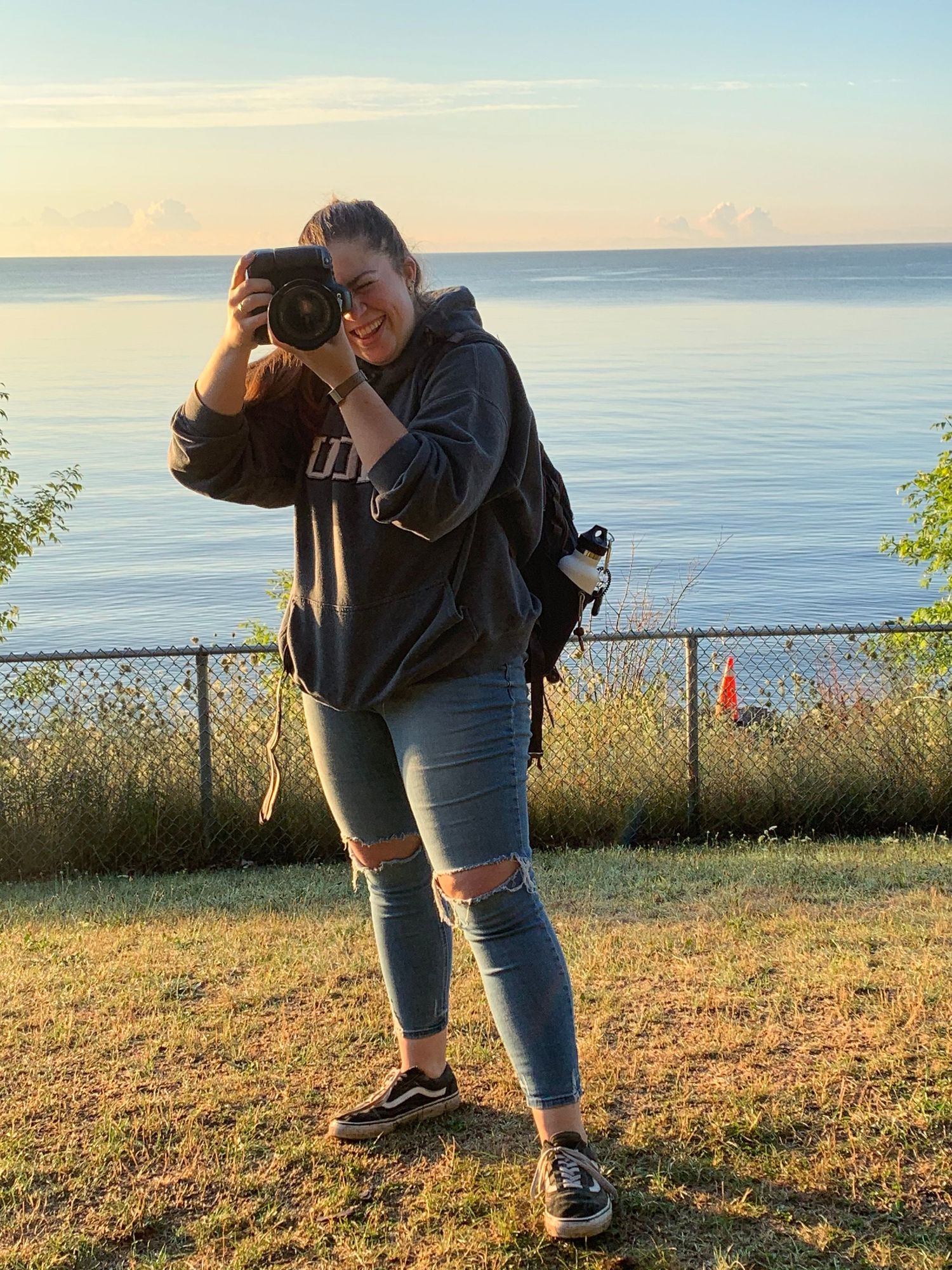 Elizabeth Mayhew Photography taking photographs with the Oshawa Lake behind her; a behind the scenes photo