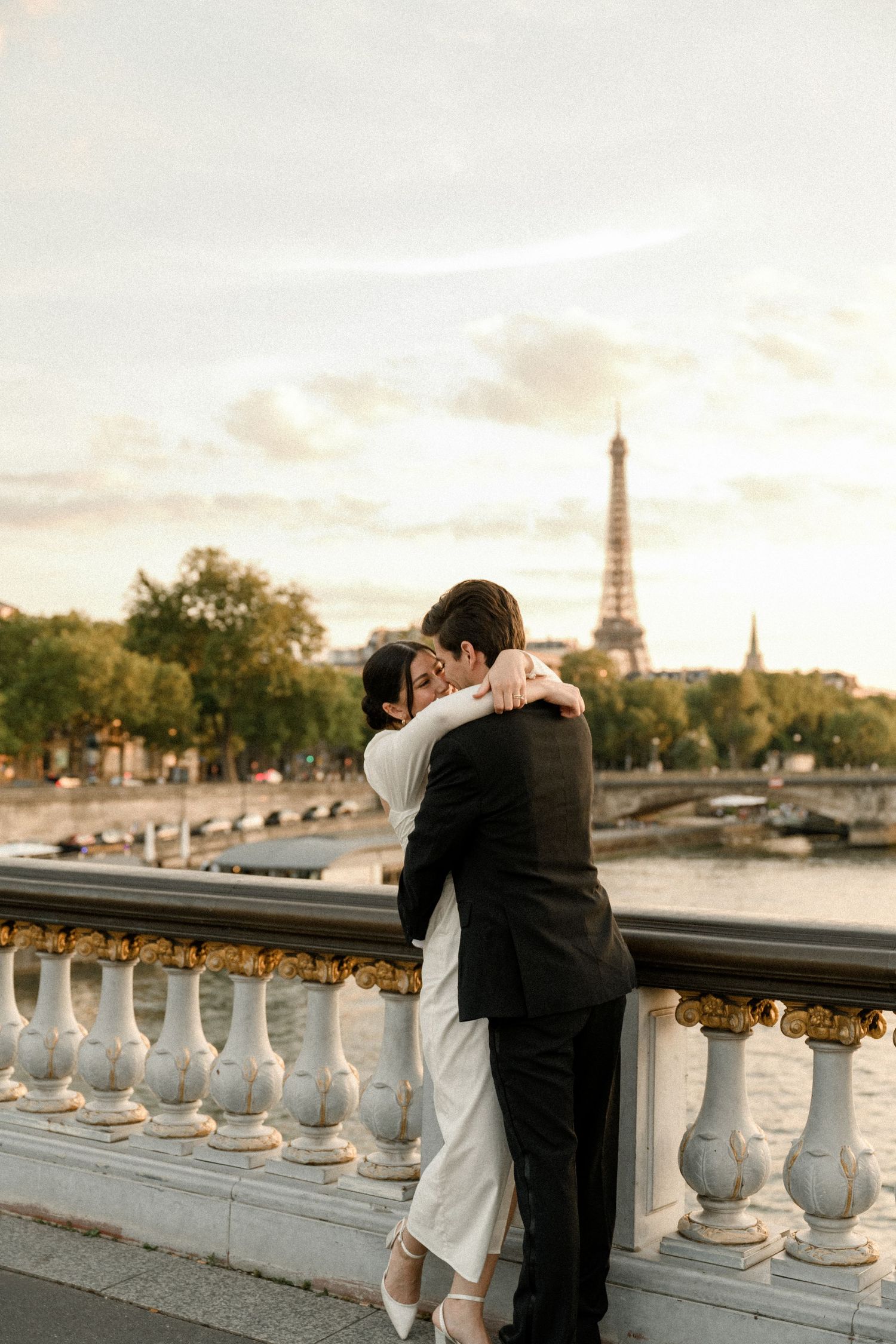 A romantic embrace overlooking the Seine River with the Eiffel Tower visible in the warm sunset light of Paris.