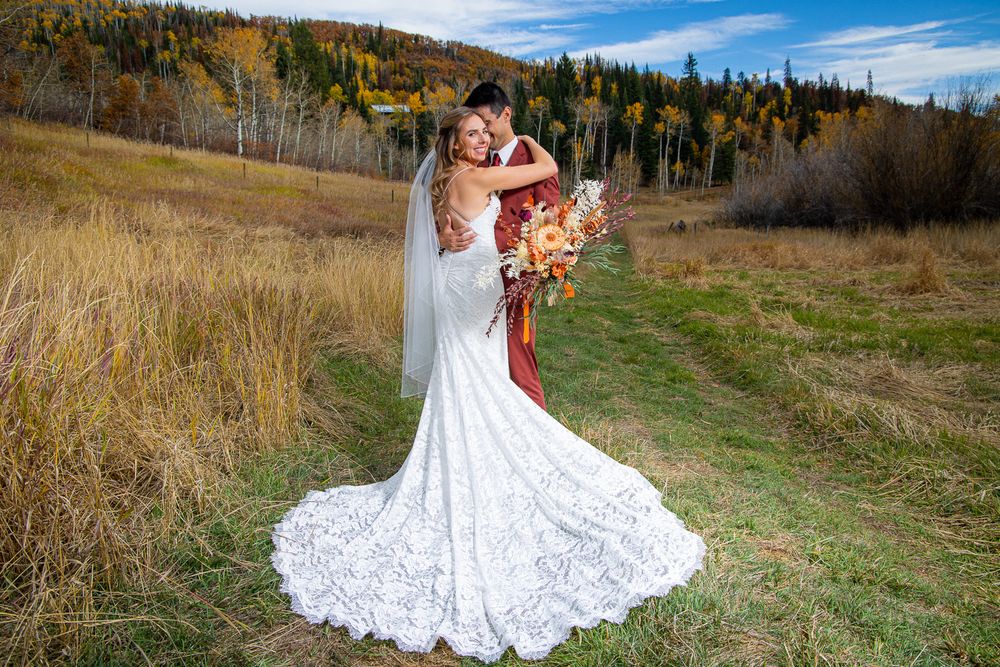 Bride in lace dress holds autumn-colored bouquet against mountain backdrop.