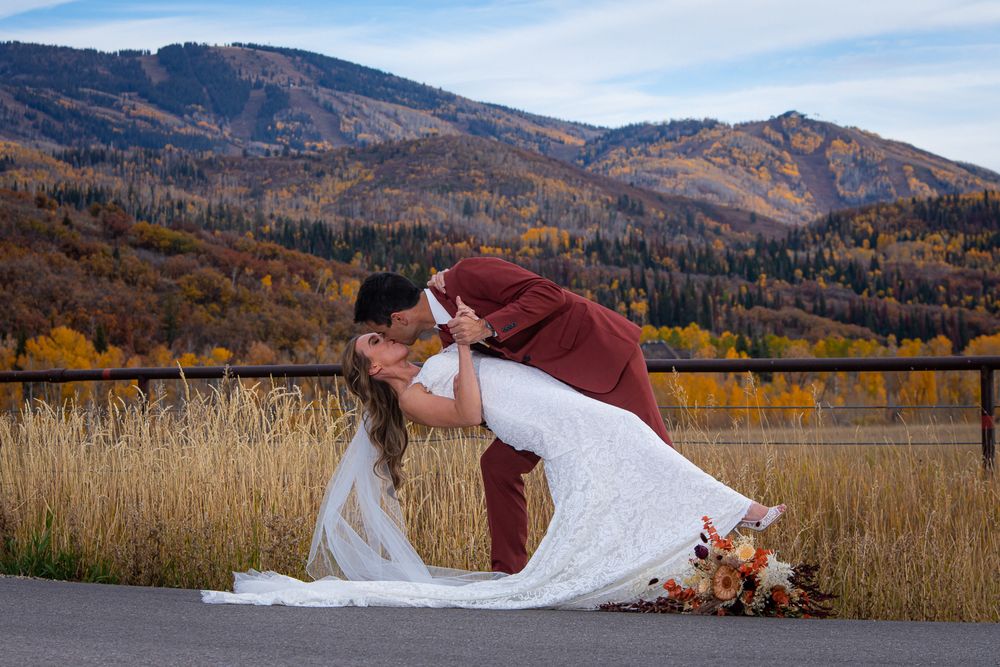 Romantic wedding couple poses for a dramatic dip in front of autumn mountain landscape.