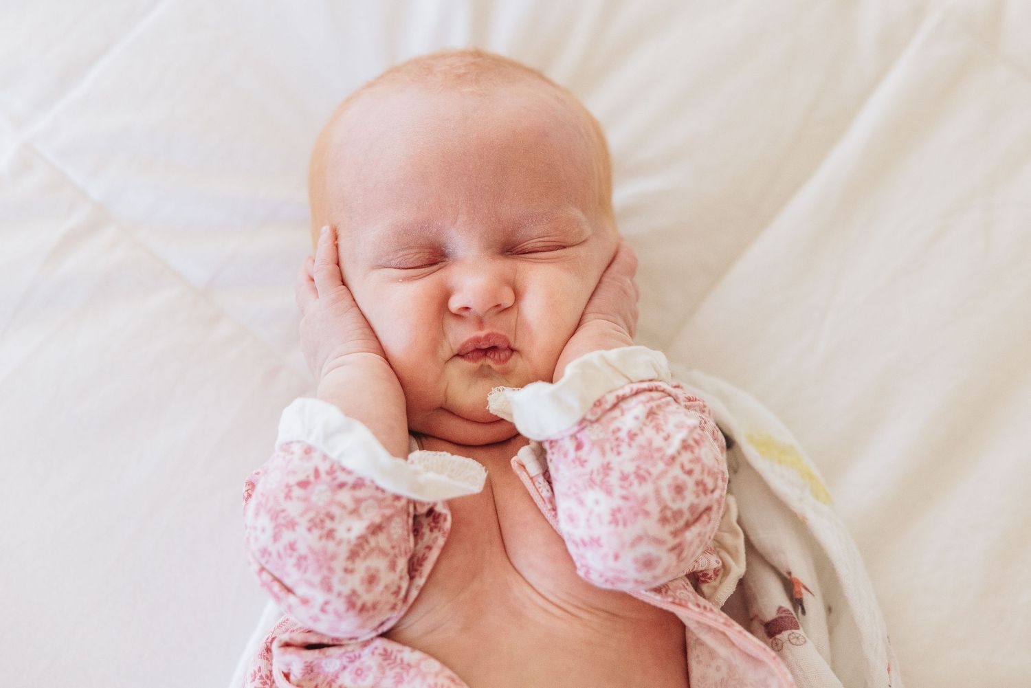 Peaceful sleeping newborn wearing pink floral outfit on white bedding.