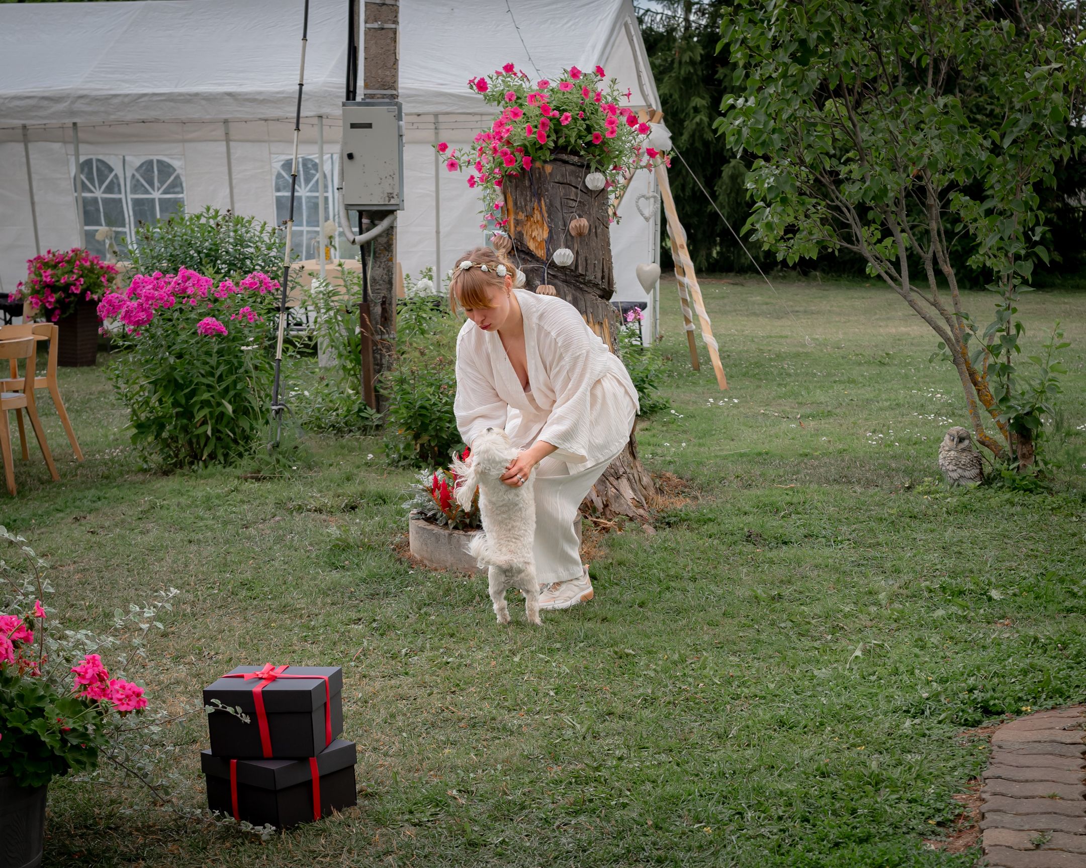 A person in formal attire poses with a gift box in a garden setting.