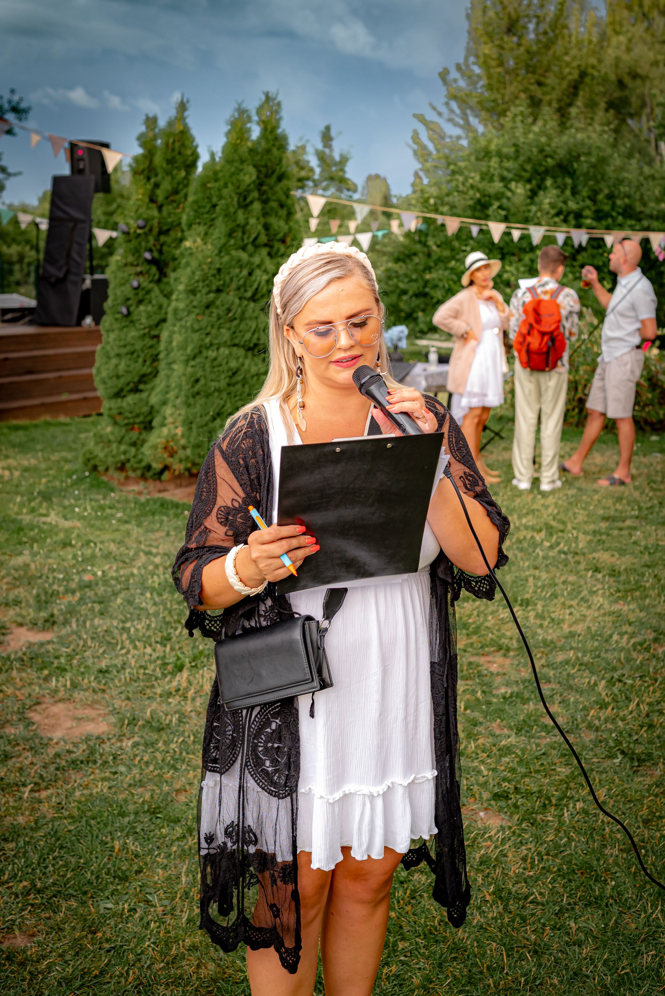 Someone reading from a document at an outdoor event wearing a black lace overlay and white dress.