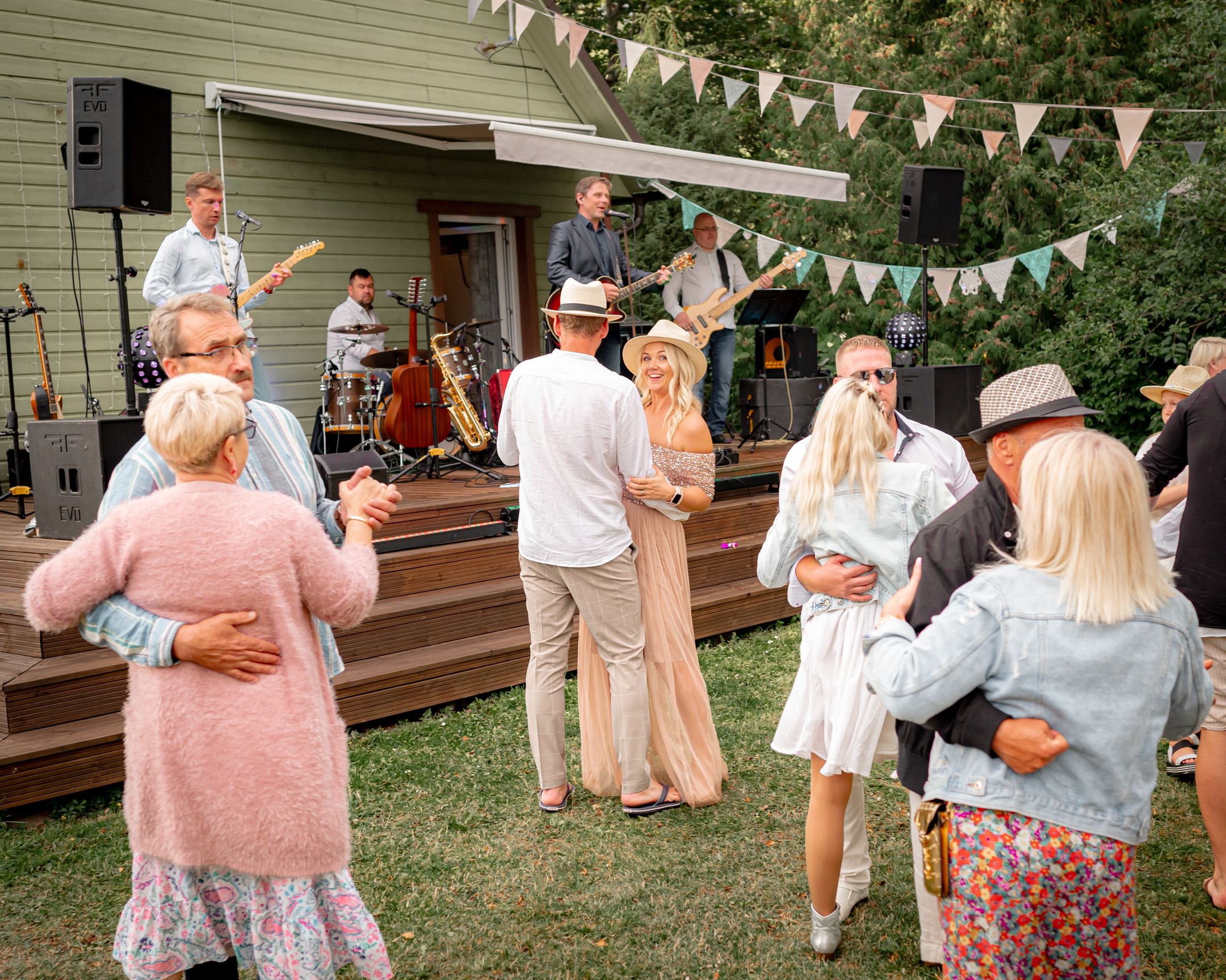 People dancing and socializing at an outdoor party with live music and bunting decorations.