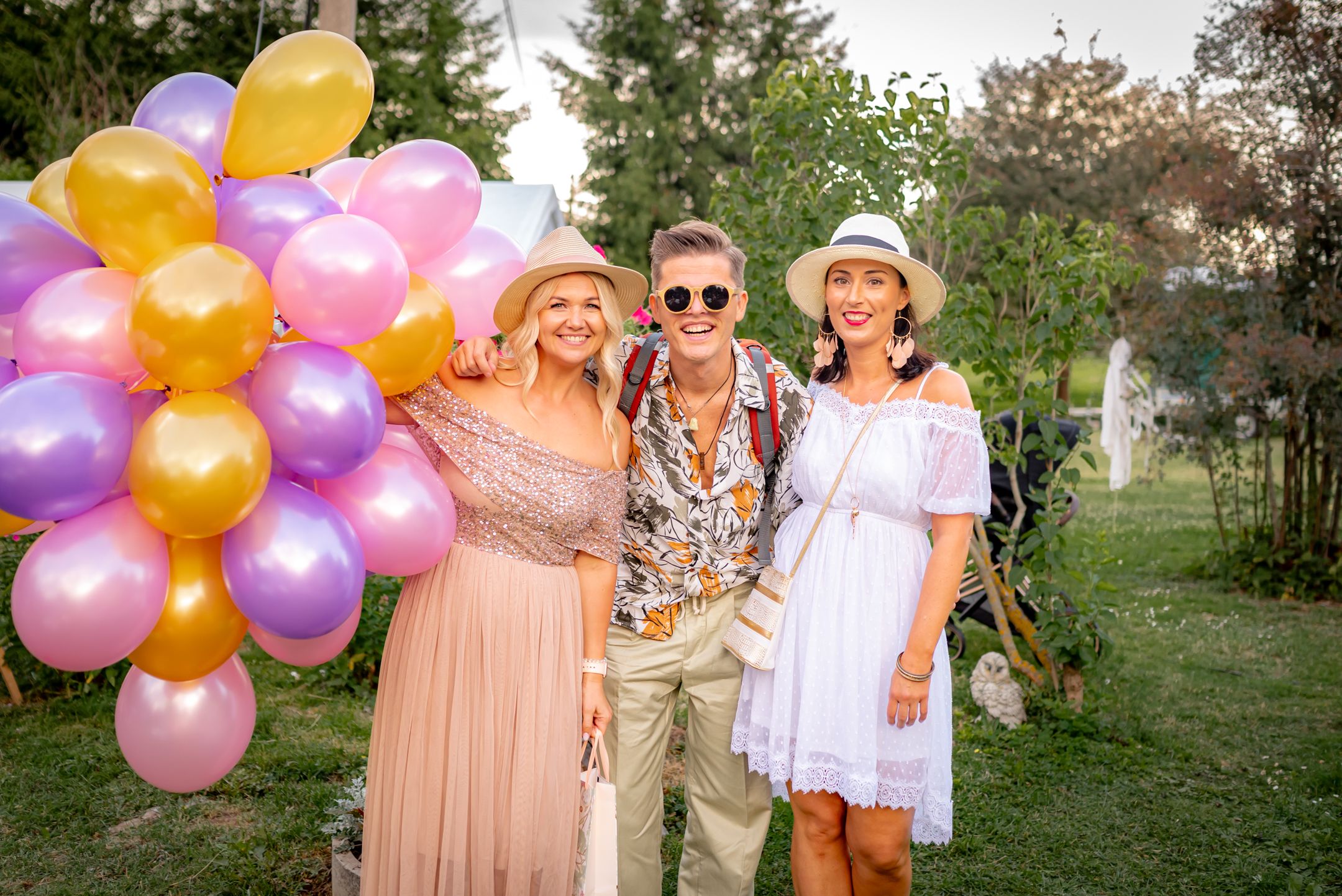 Festive outdoor party scene with colorful balloon arch and guests in summer attire.