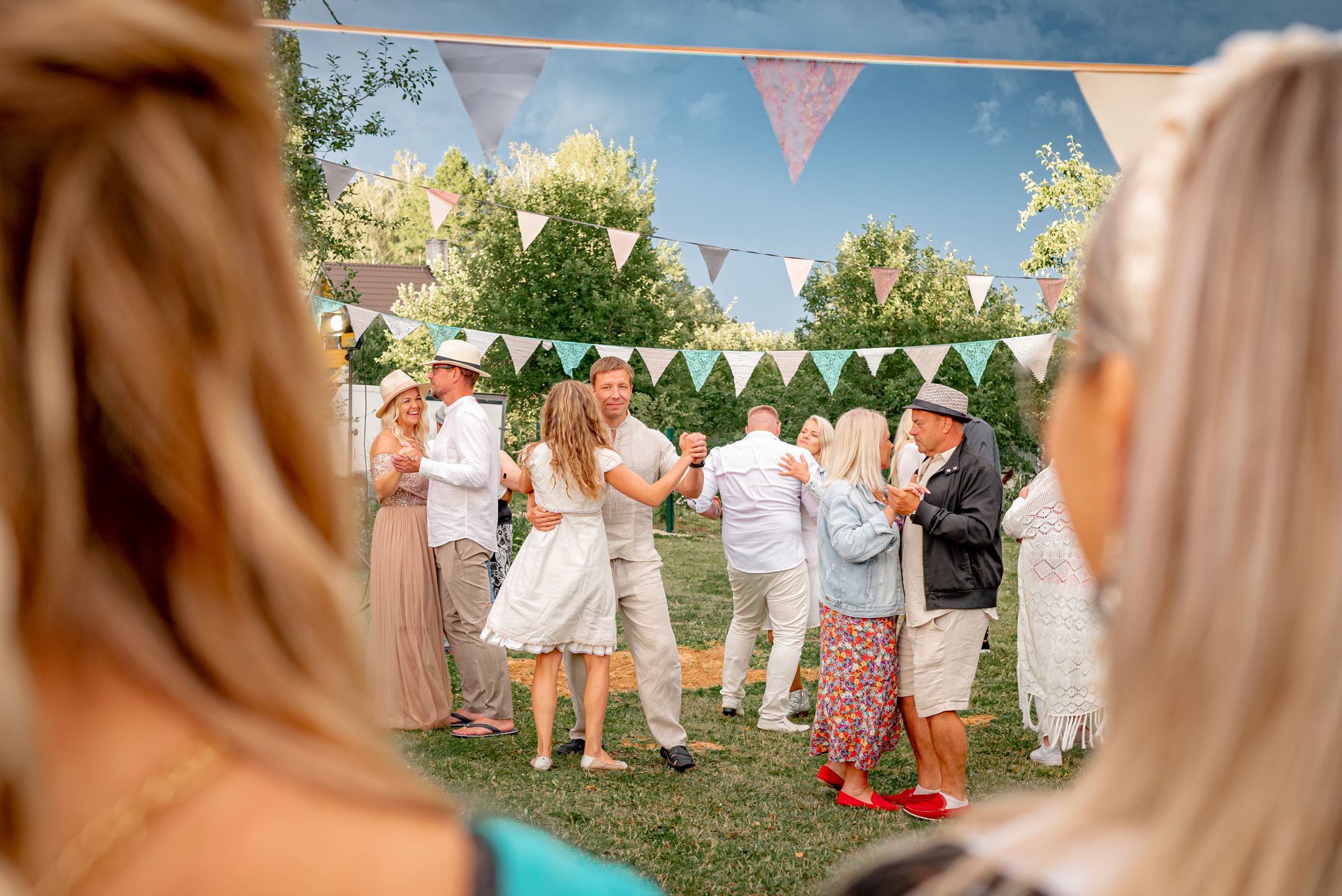 View through spectators of party guests gathered on lawn under triangle bunting decorations.