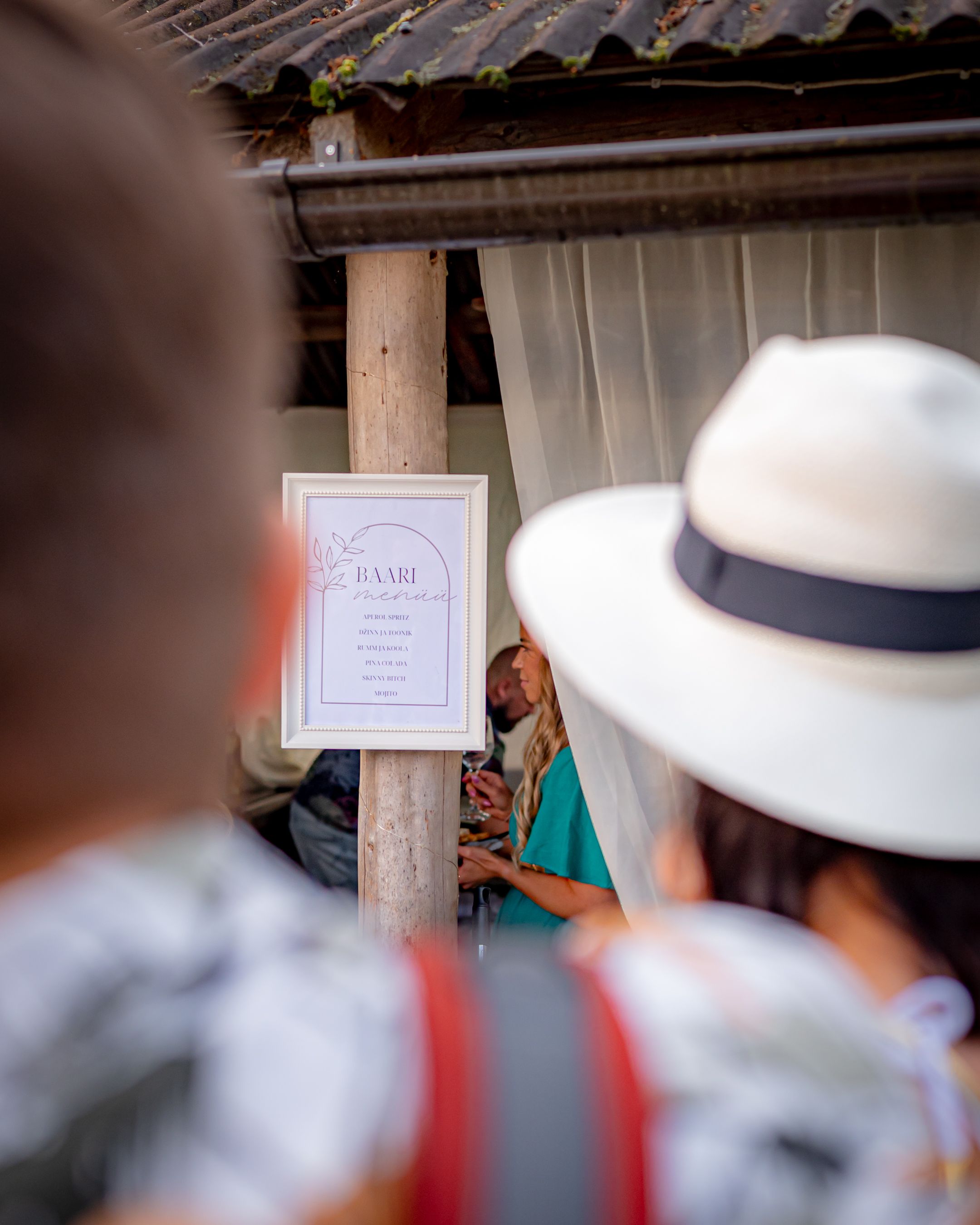 Event guests gather around a framed party menu sign at an outdoor venue.