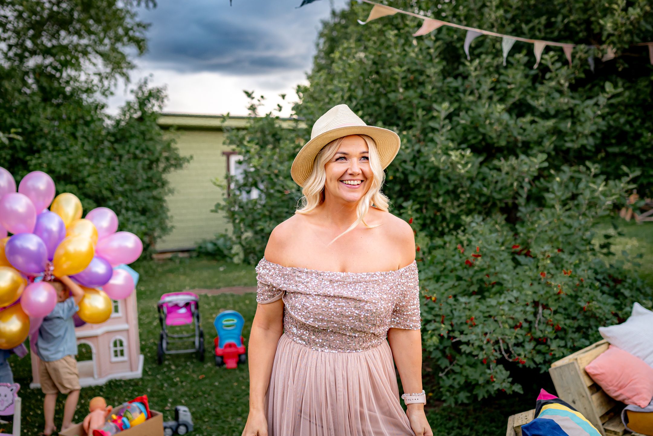 Garden party scene with balloons and decorations featuring someone in a pink dress and straw hat.