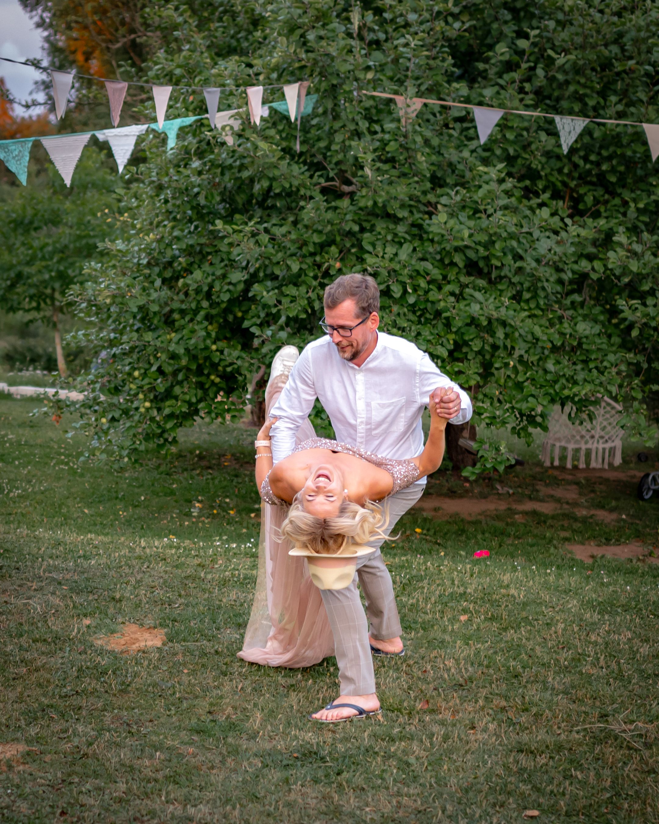 Couple performs a playful dance dip move at an outdoor party with bunting decorations.