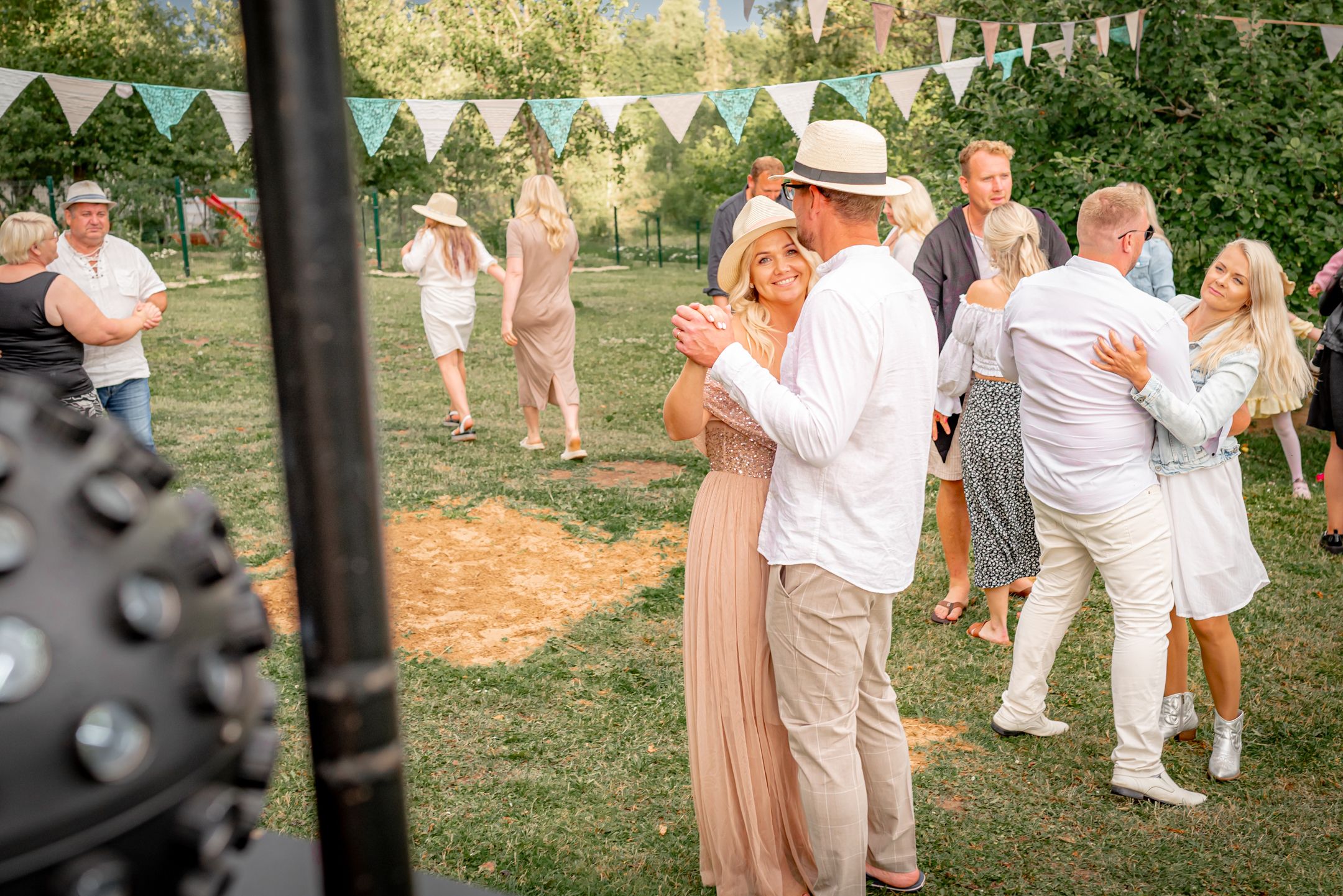 Garden party scene with couples dancing on grass under white triangle bunting.