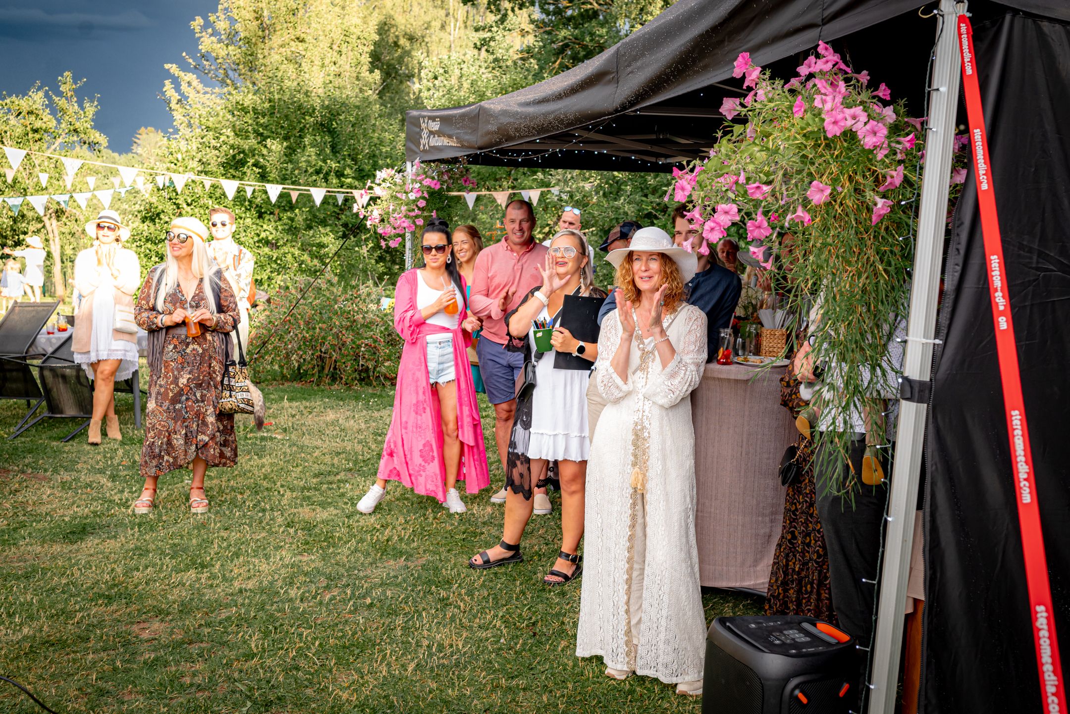 Outdoor summer party with attendees gathered under a tent with pink floral decorations.