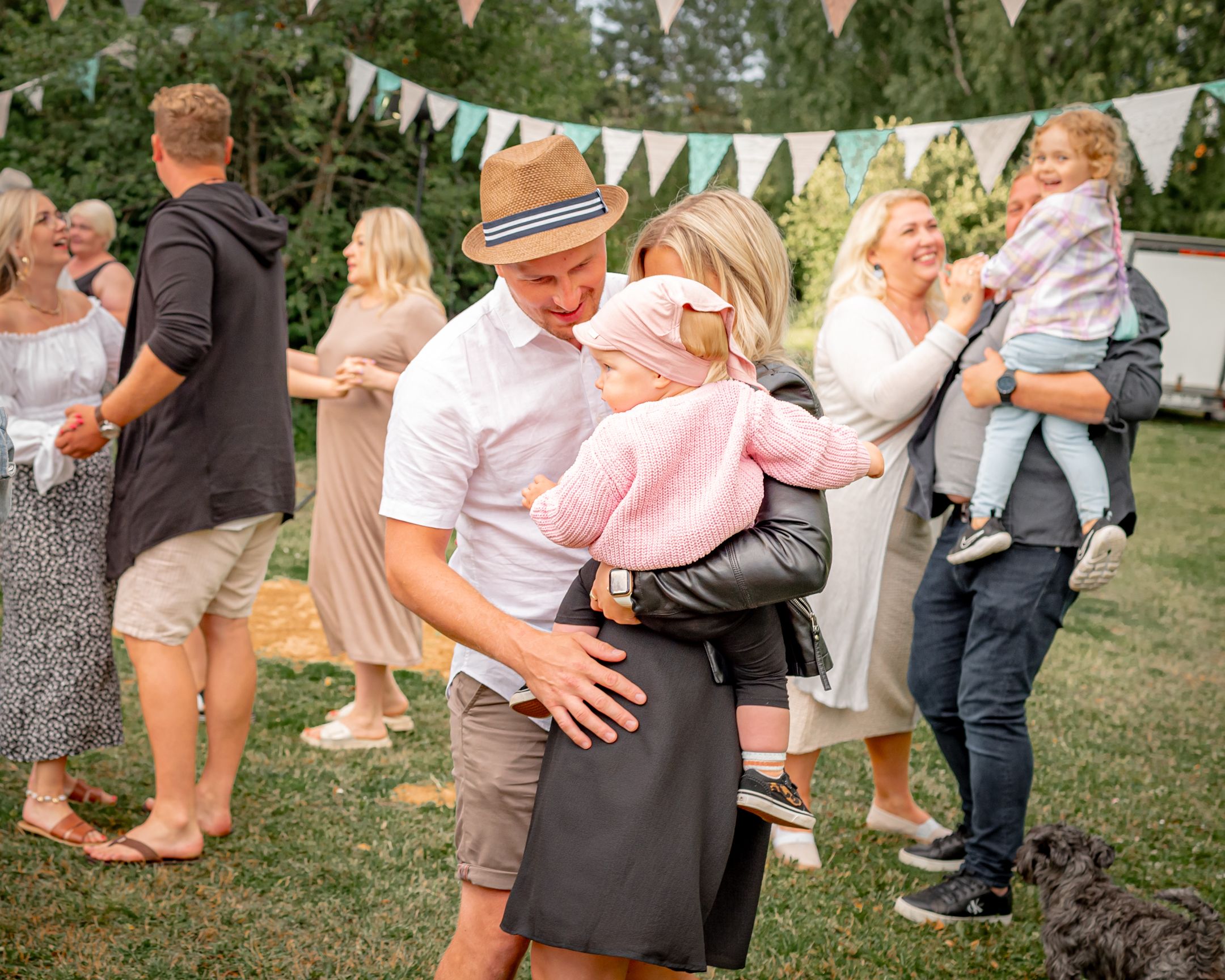Outdoor garden party with people dancing and mingling under white bunting decorations.
