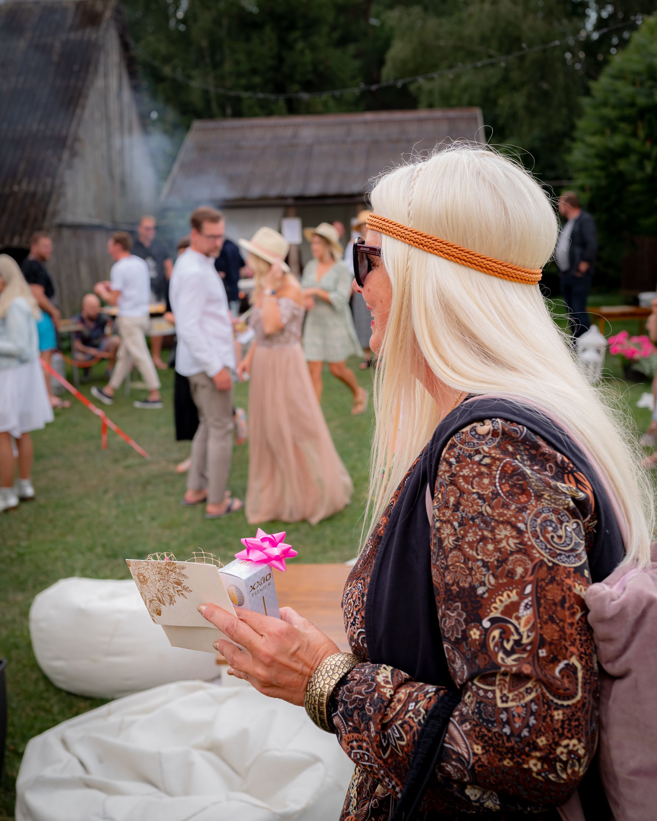 A guest in boho attire reads a card during an outdoor summer celebration.