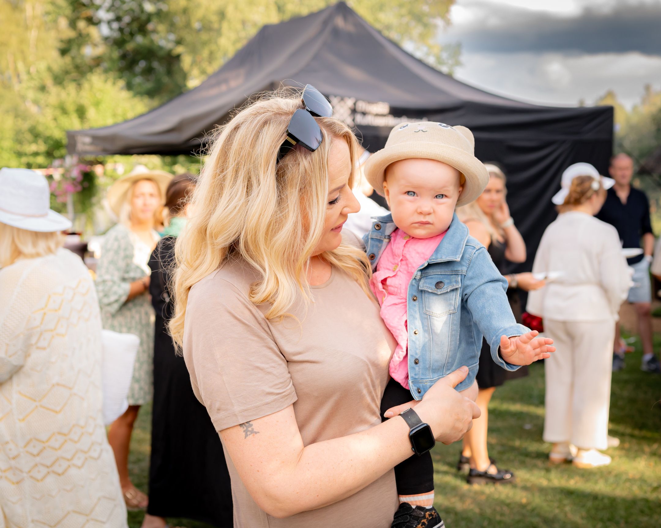 An outdoor summer celebration with guests under a black tent canopy.