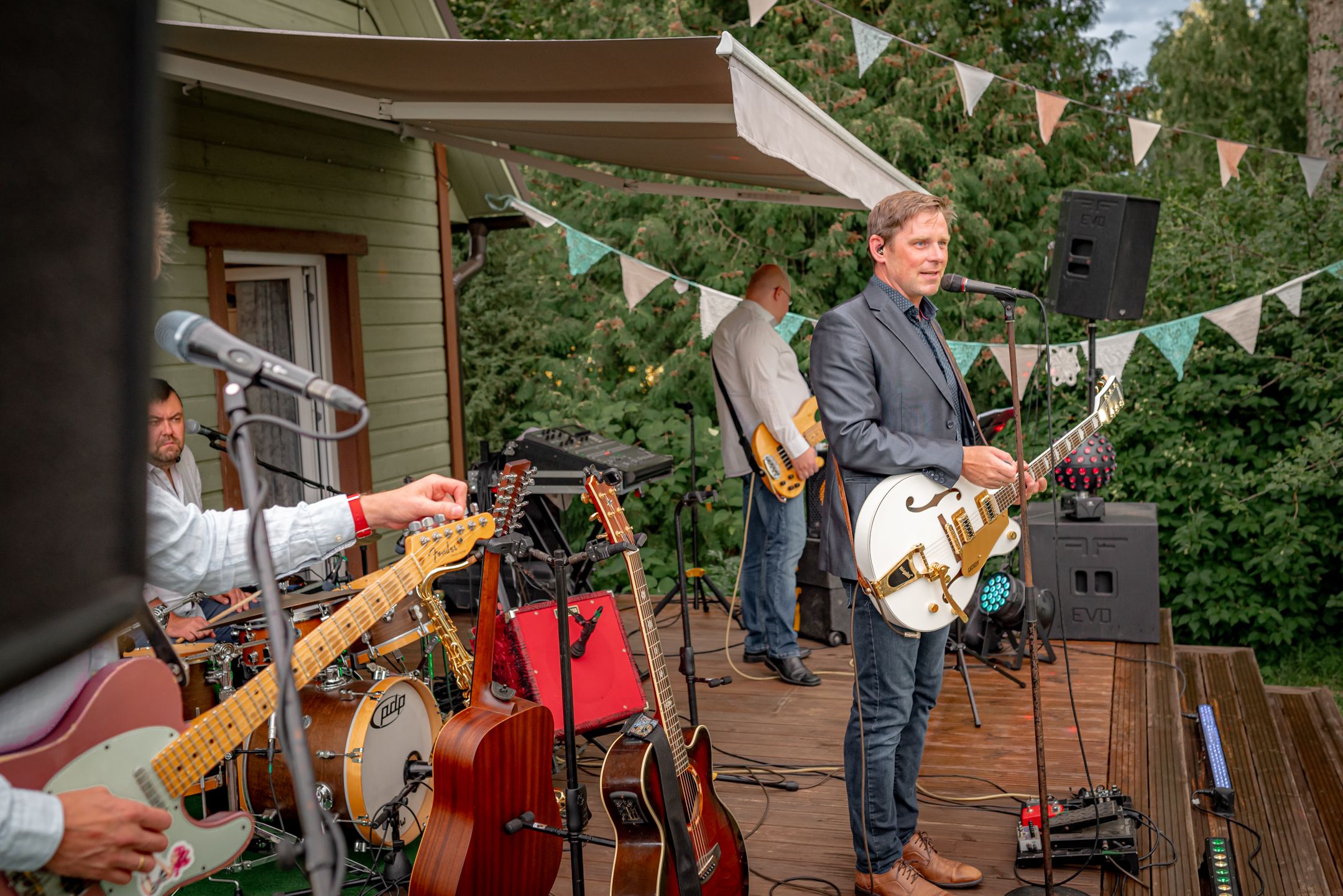 Musicians performing on an outdoor deck with guitars and equipment setup.
