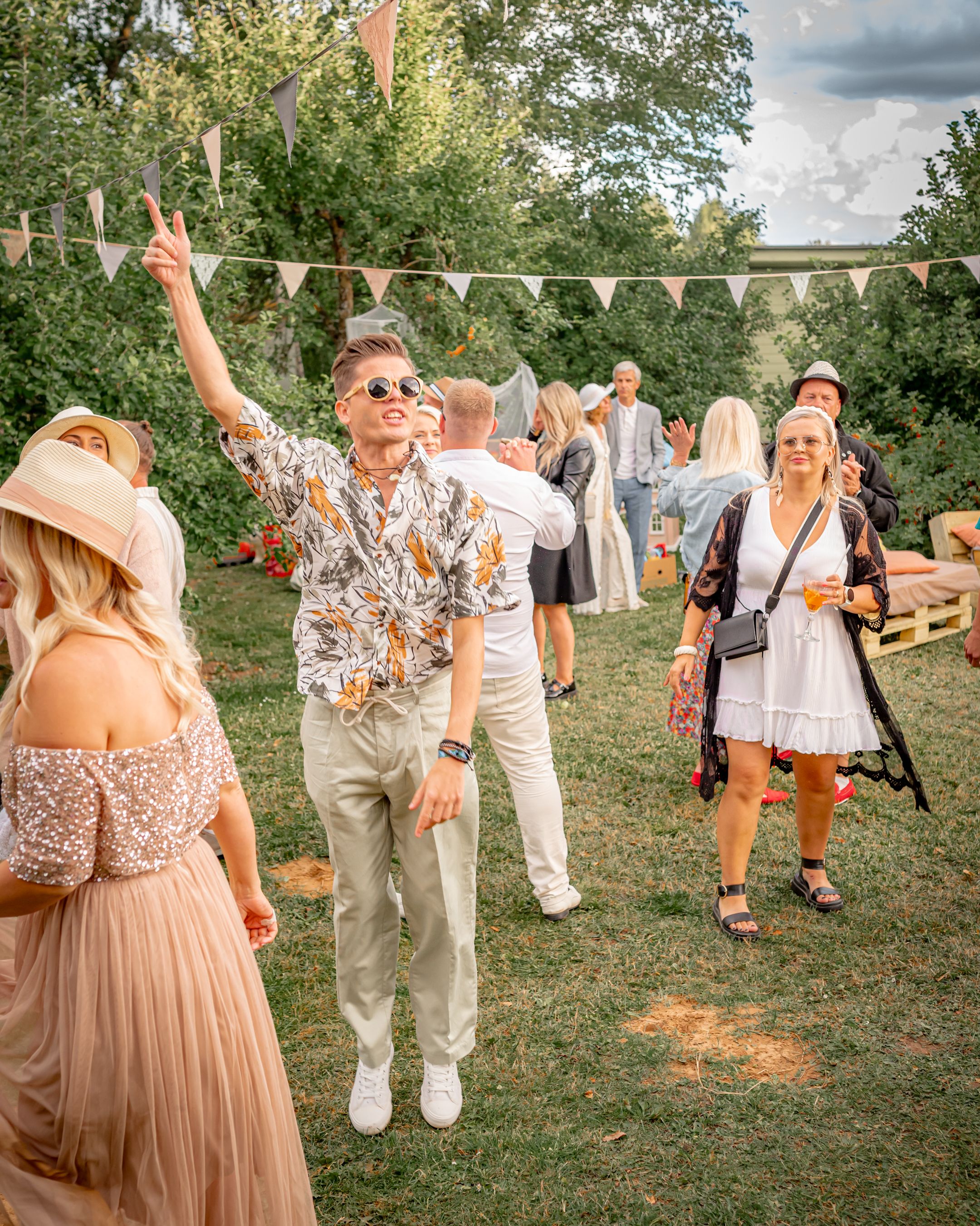 Energetic party scene with guests dancing and celebrating under decorative bunting in a garden setting.