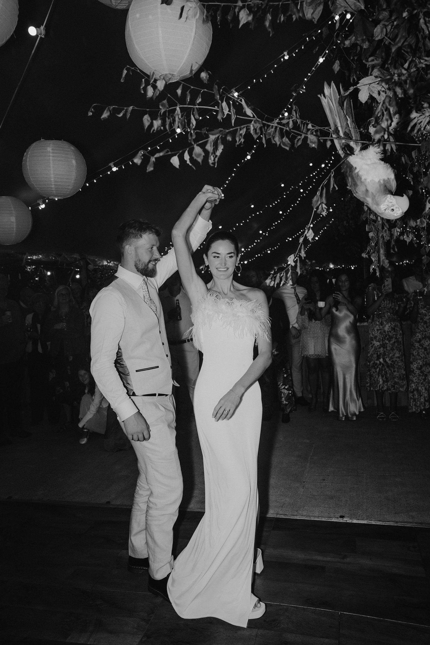 groom twirling bride underneath fairy lights and lanterns during first dance in marquee in oxfordshire