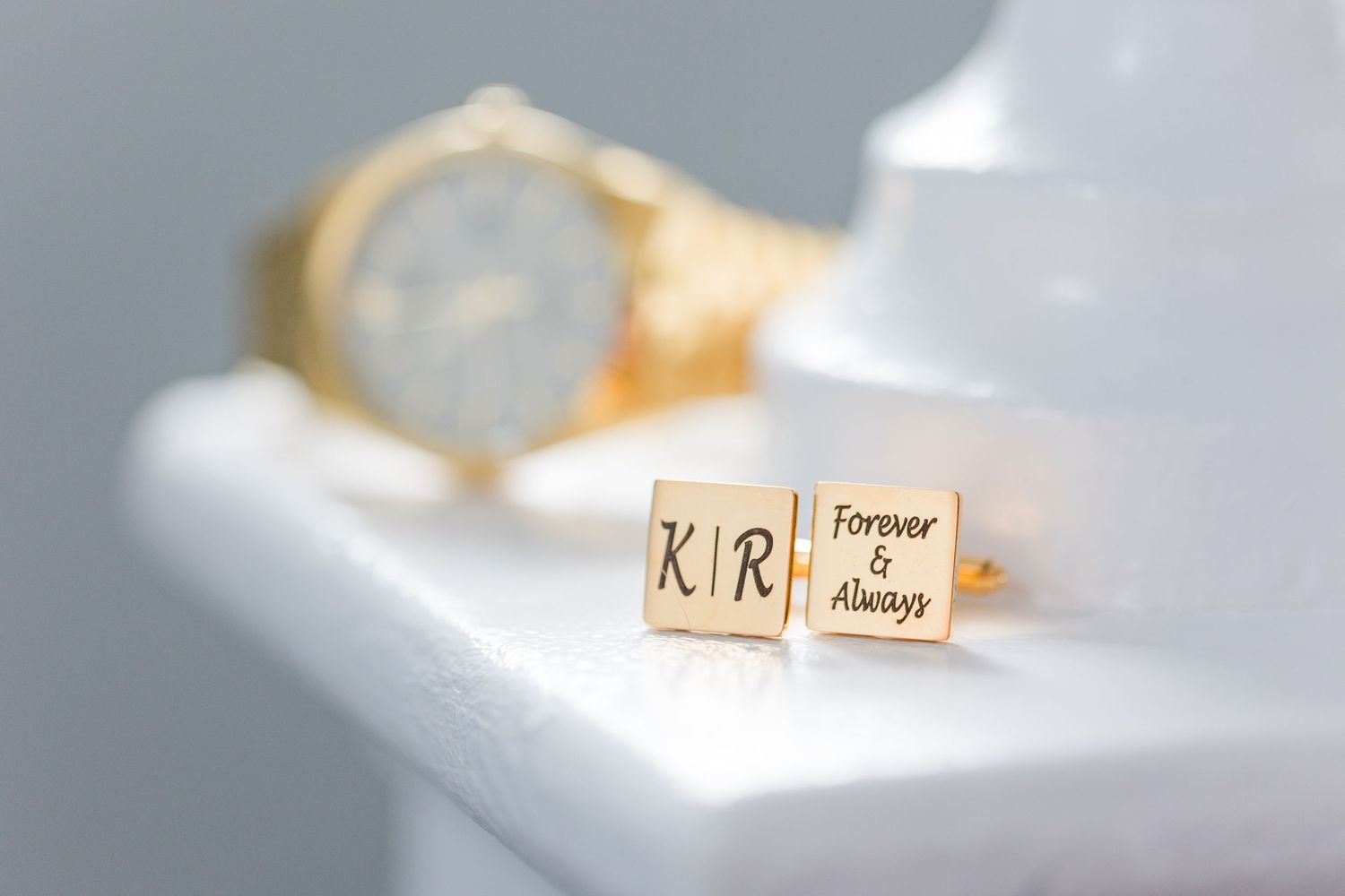Close-up of gold wedding cufflinks with initials on white surface.