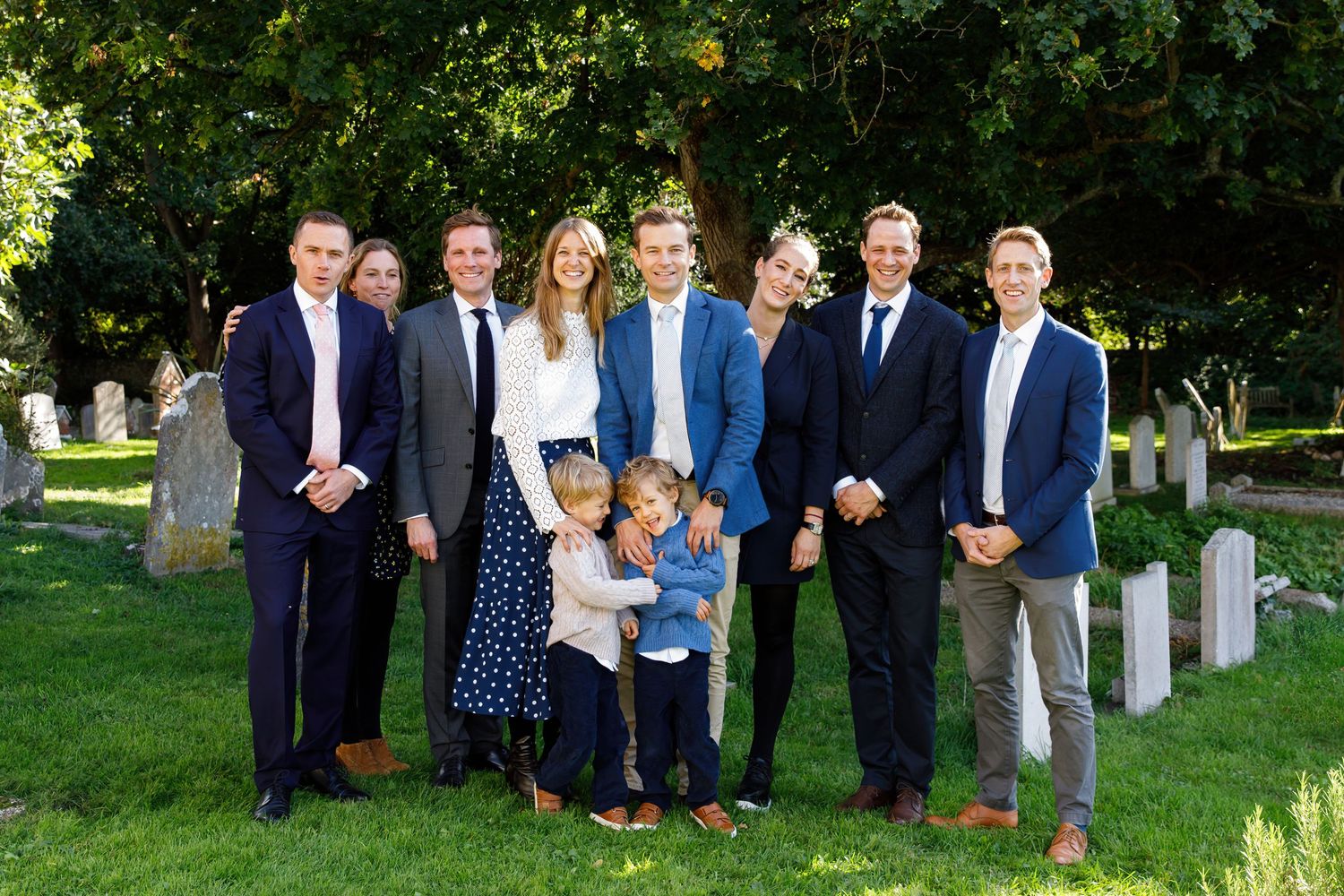 Large family gathering for a formal portrait in a garden setting with headstones.