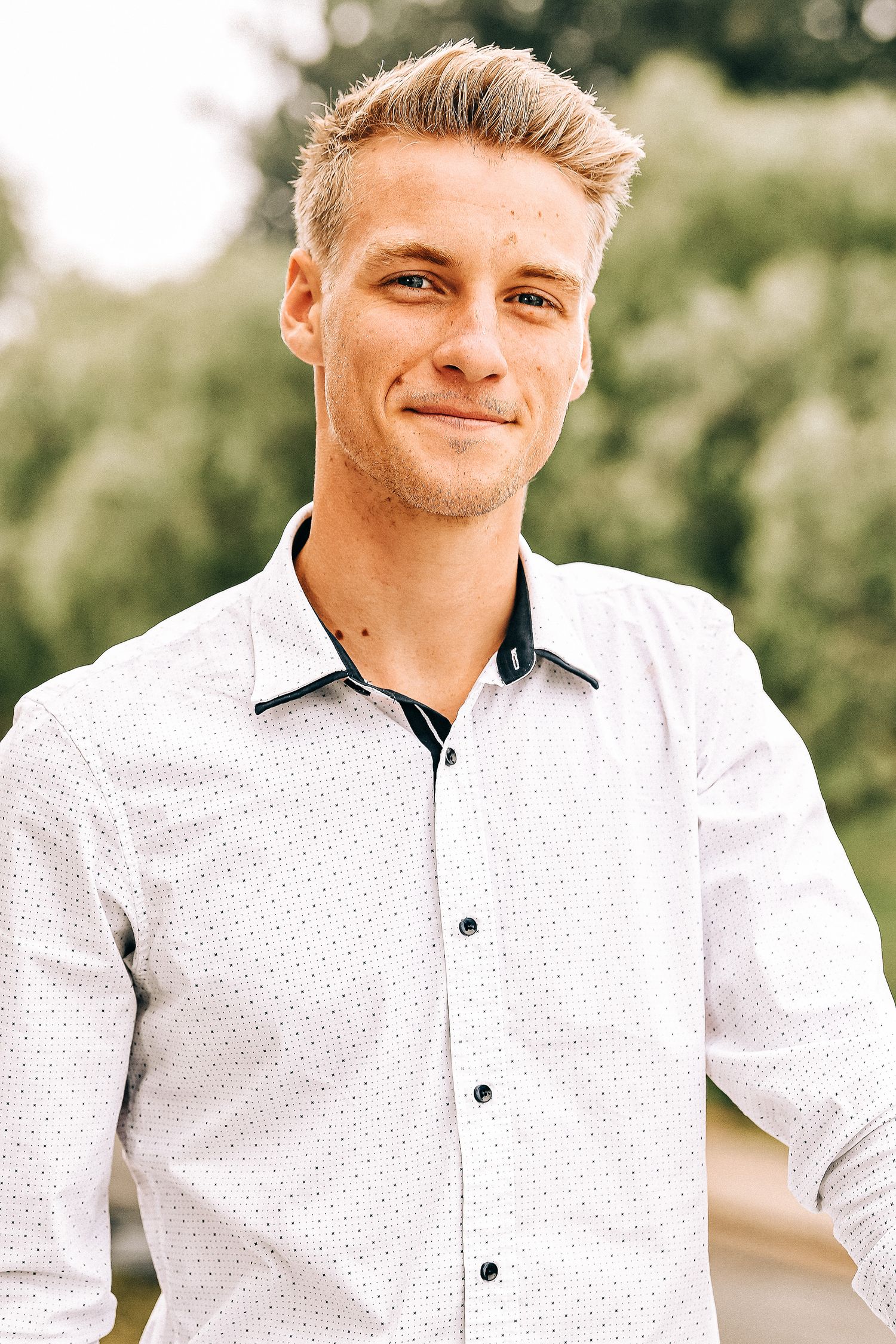 Portrait of someone wearing a white polka dot dress shirt outdoors.