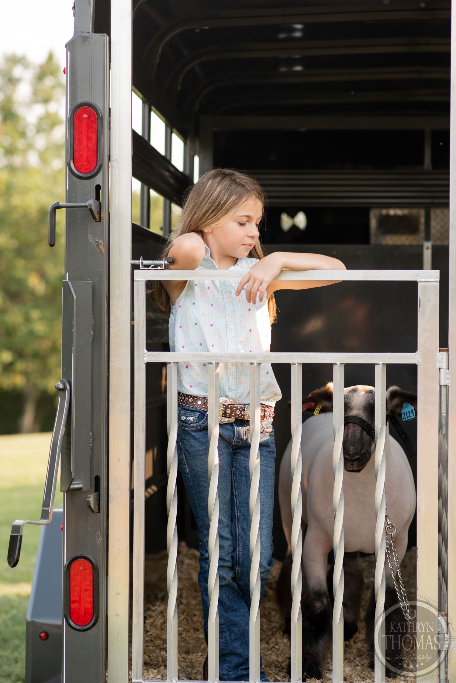 Person leans on horse trailer gate with horses visible inside during sunset.