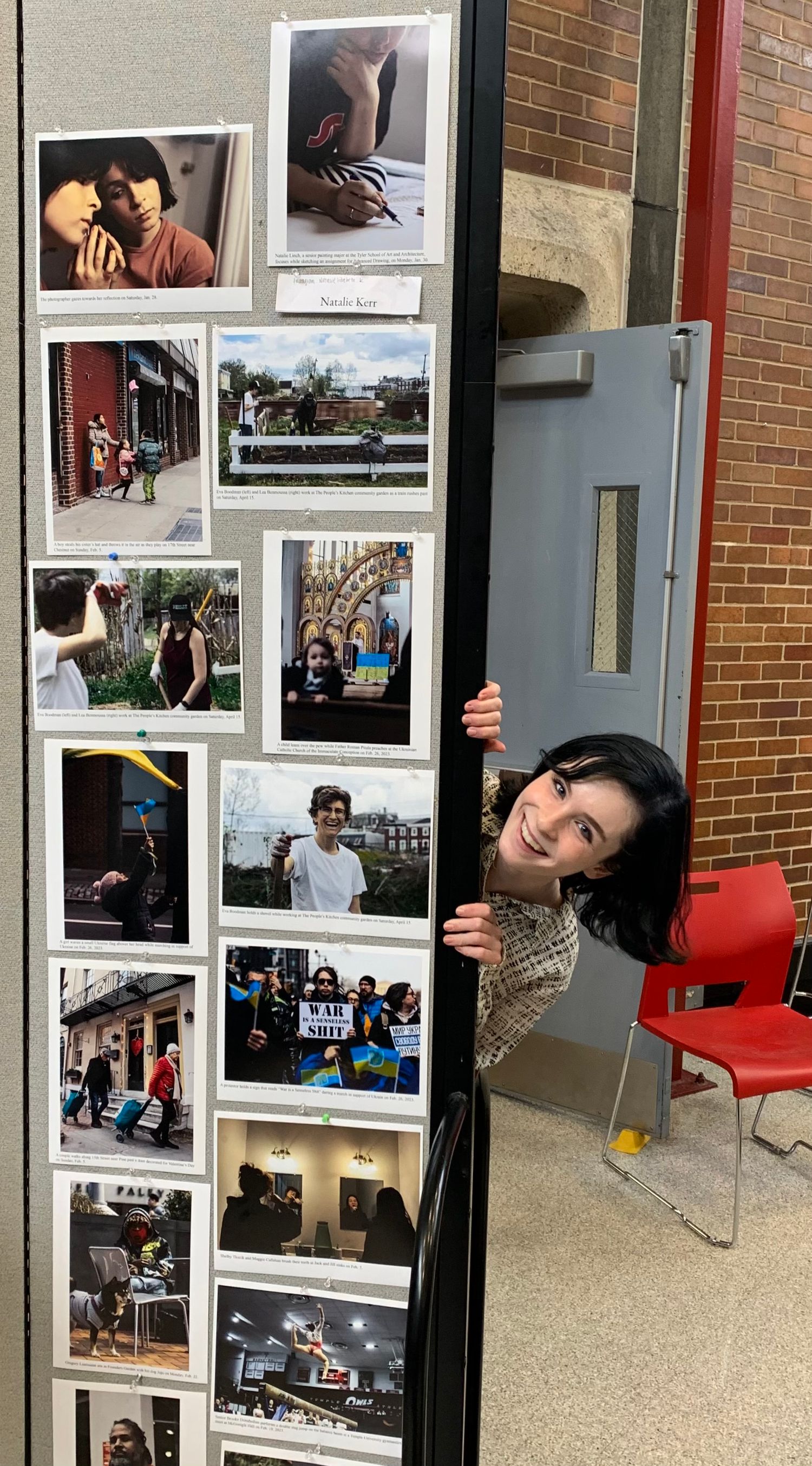 Natalie peaking out from behind a gallery of her photos