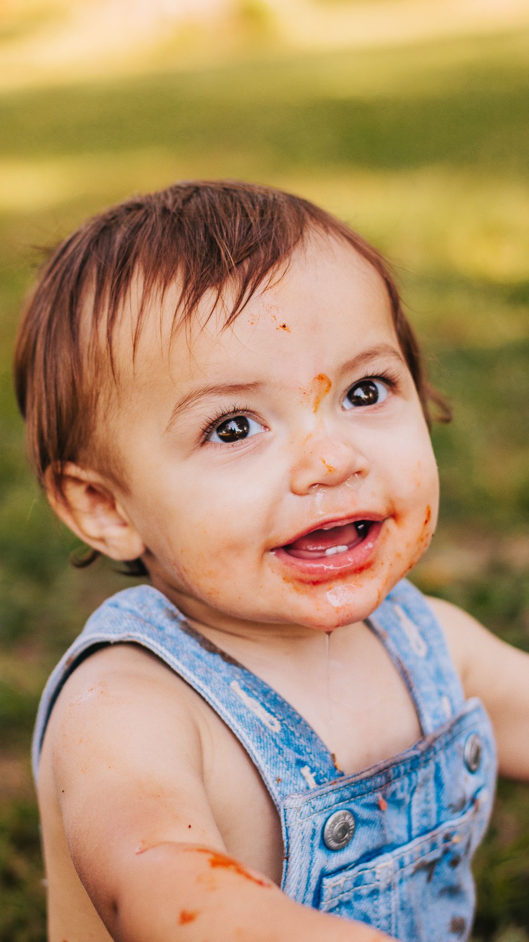 Baby in blue overalls with messy face smiling at camera.